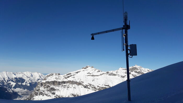 Climate station on an alpine summit: solar panel, sonic anemometer, modem enclosure, solar-autonomous at high altitude.