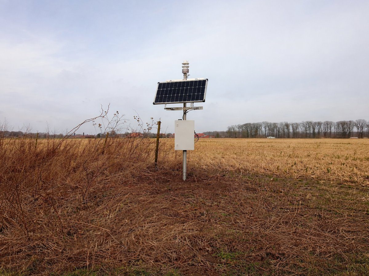 Klimaatstation met zonnepaneel en weersensor op een geoogst veld in de nawinter