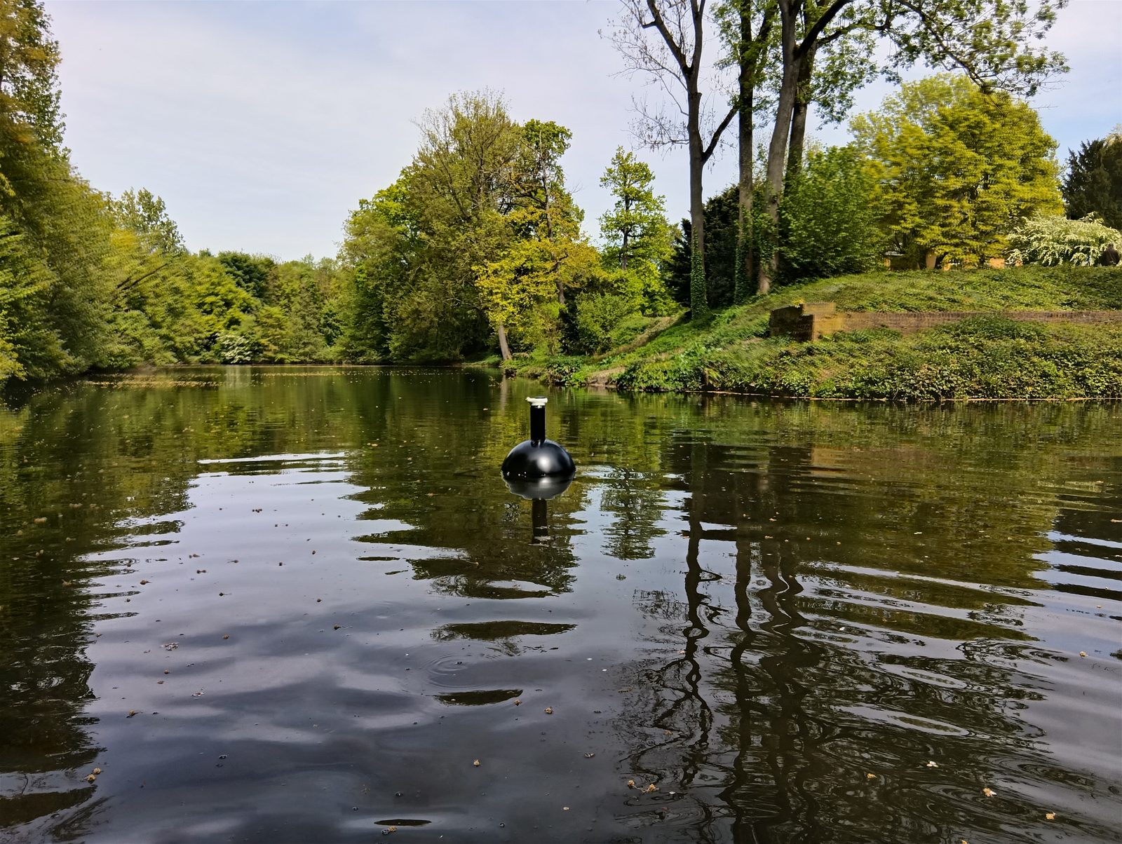 Zwarte meetboei drijvend op een rustige parkvijver in het voorjaar