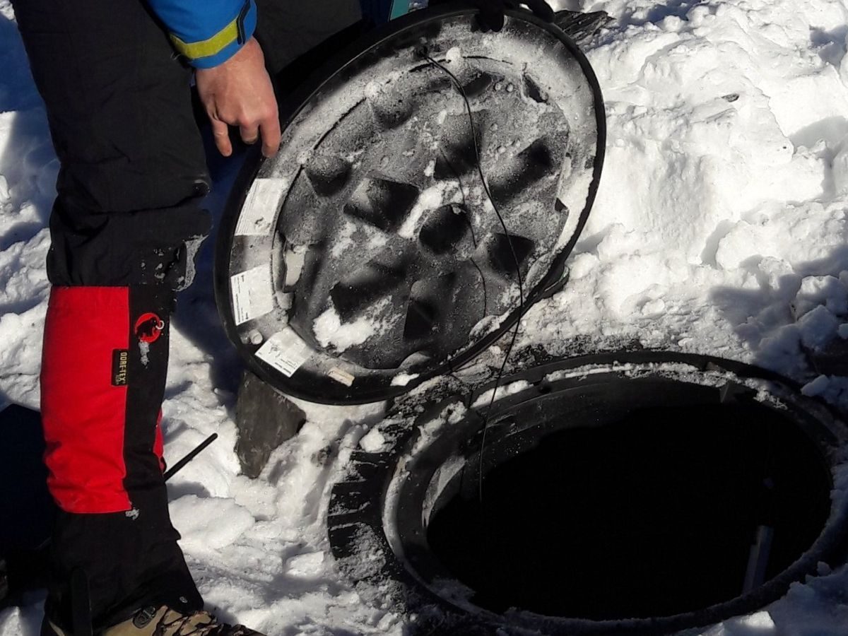 Monteur tilt een putdeksel op in de sneeuw, de temperatuurketting wordt eruit gehaald