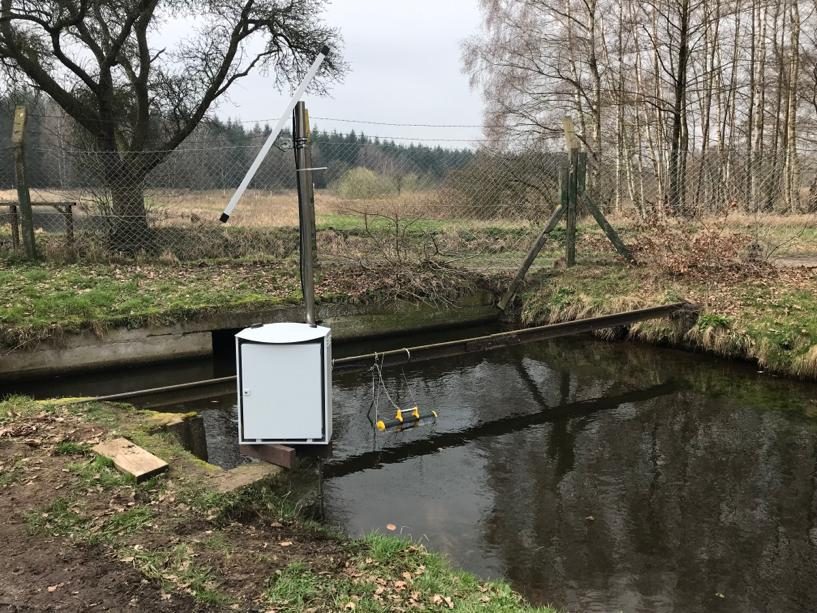 Peilkast aan een omheinde watergang in de heide, meetapparatuur in beschermkast