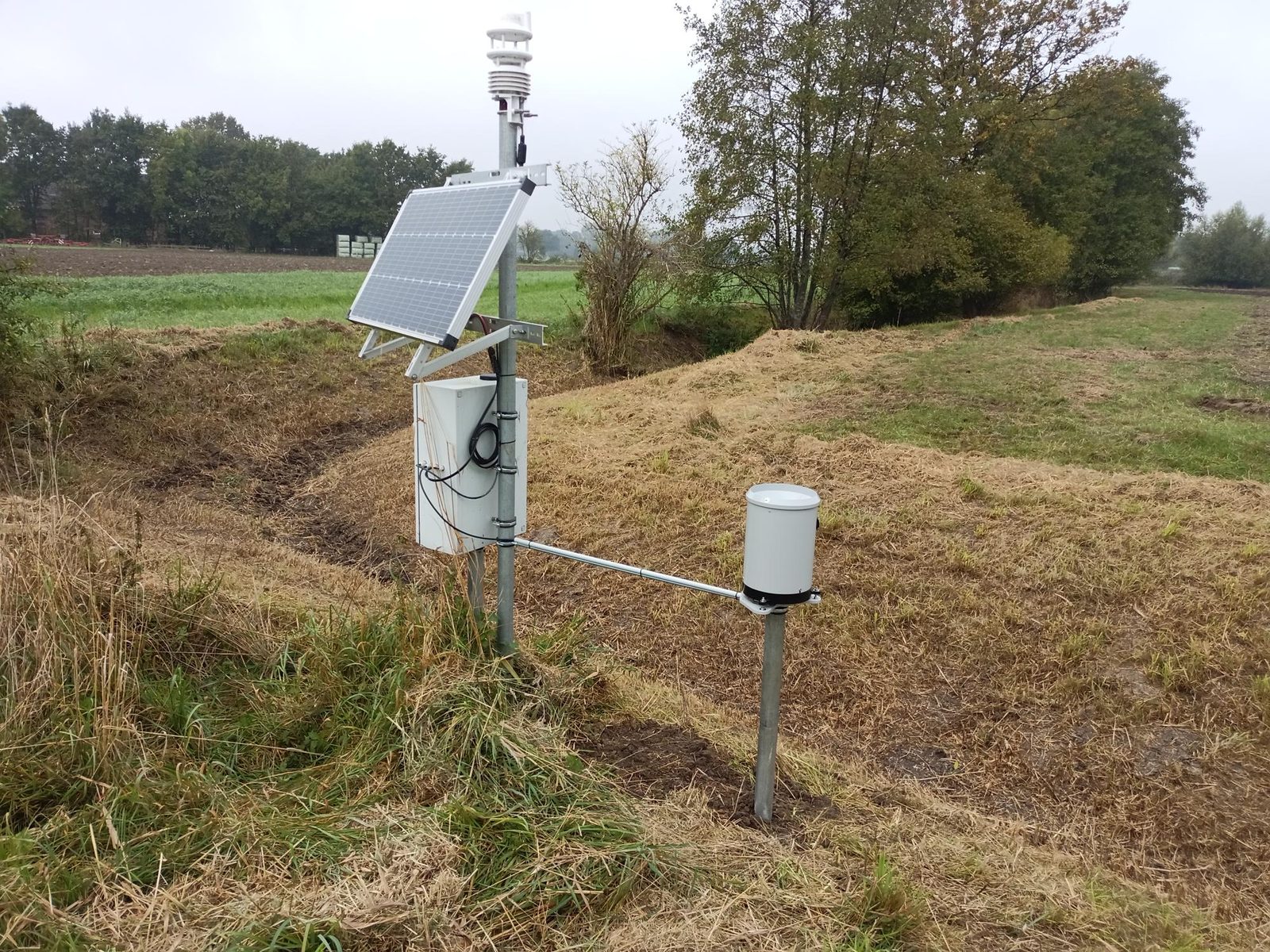 Klimaatstation met regensensor en zonnepaneel aan de veldrand bij herfstweer