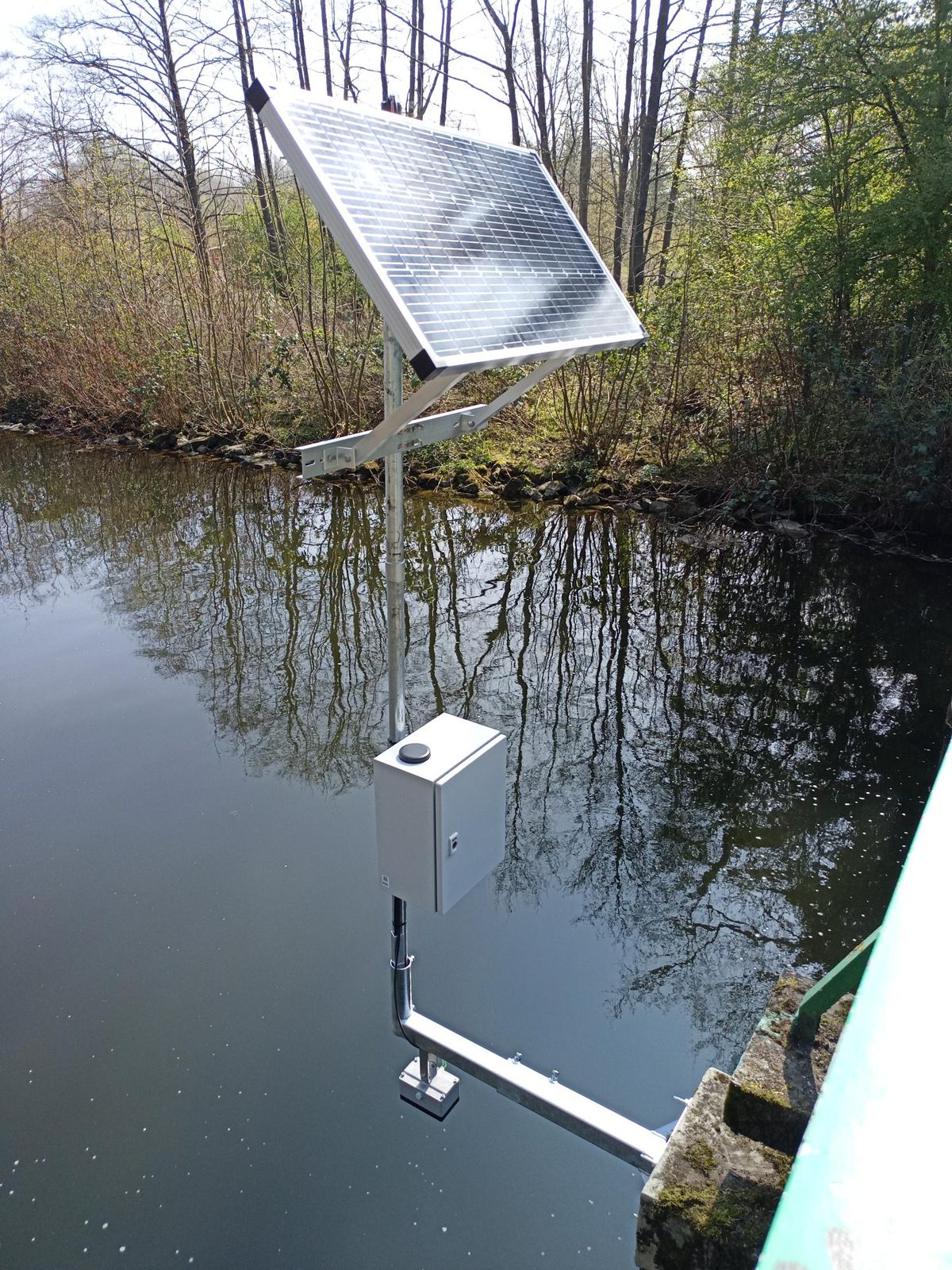 Verhoogde zonnepaneel-arm boven een bosvijver, datalogger boven het wateroppervlak