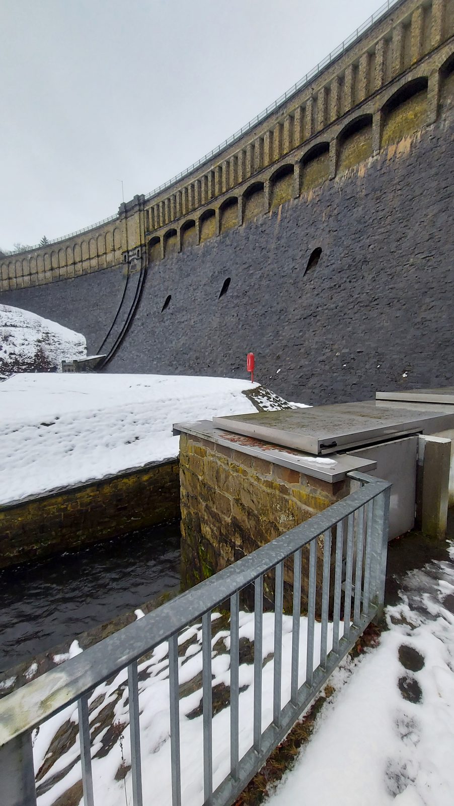 Natuurstenen stuwdam met uitlaat in de winter, peilstation aan de muurvoet